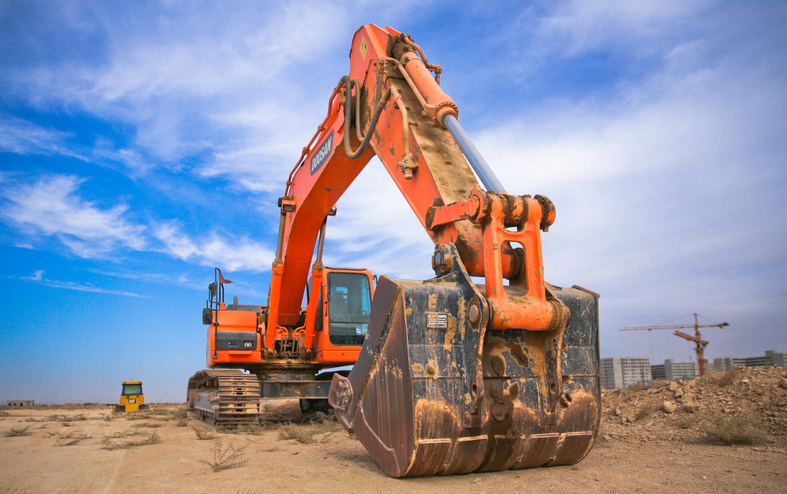 Home A large orange excavator working on a construction site under a blue sky.